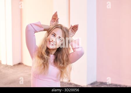 Joyeuse jeune femme caucasienne posant de manière ludique sur fond rose Banque D'Images