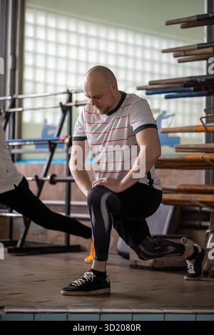 Le rameur concentré motivé s'étire en squat, activant les muscles avant l'entraînement intense d'aviron Banque D'Images