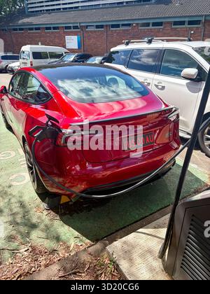 Véhicule électrique Tesla Model 3 rouge 2024 chargé sur un chargeur Jolt public à Mona Vale, Sydney, Australie Banque D'Images