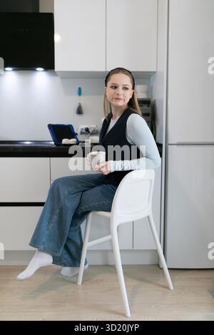 Jeune femme profitant d'une boisson chaude tout en étant assise sur une chaise dans une cuisine moderne pendant la matinée Banque D'Images
