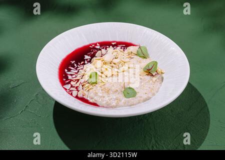 Délicieux bol de flocons d'avoine crémeux surmonté de sauce aux baies, d'amandes et d'herbes fraîches sur un fond vert vif Banque D'Images