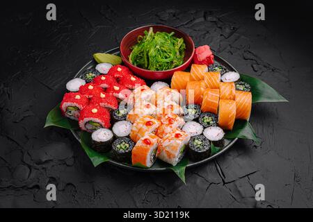 Délicieux plateau de sushi avec divers rouleaux et côtés sur une surface texturée sombre Banque D'Images