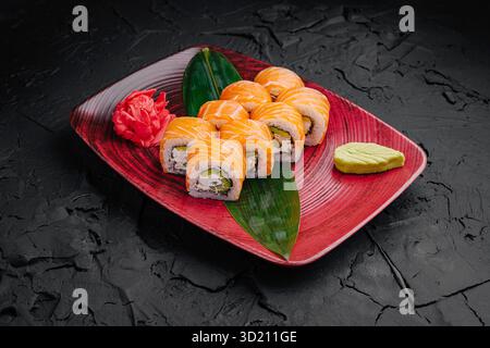 Plateau de sushi avec rouleaux de saumon disposés artistiquement sur une surface noire texturée Banque D'Images