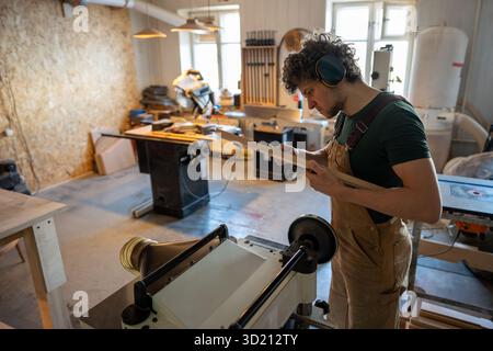 Bricoleur professionnel sérieux mesure l'épaisseur de la planche de bois avec des étriers dans l'atelier de meubles Banque D'Images