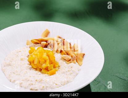 Délicieux bol de flocons d'avoine garni de mangue fraîche et de noix de coco grillée sur une surface verte vibrante Banque D'Images
