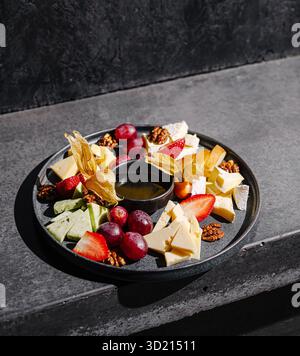 Plateau de fromage et de fruits servi sur une élégante assiette noire pour une expérience gastronomique Banque D'Images