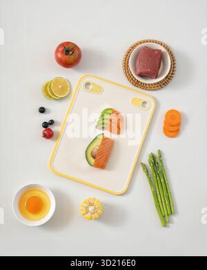 Ingrédients crus frais sur planche à découper jaune, y compris saumon avocat légumes de bœuf et fruits fond blanc photo stock Banque D'Images