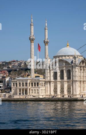 Mosquée Ortaköy s'élevant du Bosphore à Istanbul sous un ciel dégagé avec drapeau turc agitant Banque D'Images