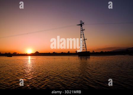 Coucher de soleil pittoresque sur une rivière calme avec une tour de transmission silhouette Banque D'Images