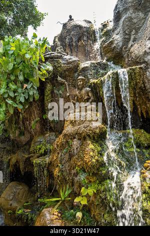 Cascade artificielle en cascade sur des rochers et des statues dans une végétation luxuriante Banque D'Images