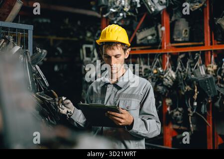 Technicien ouvrier masculin travaillant dans l'entrepôt d'atelier de vieil atelier de pièces de voiture de cour de ferraille de garage Banque D'Images
