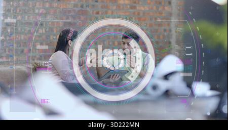 Discuter femme hispanique et homme indien examinant tablette sur canapé dans le salon, avec superposition d'interface Banque D'Images