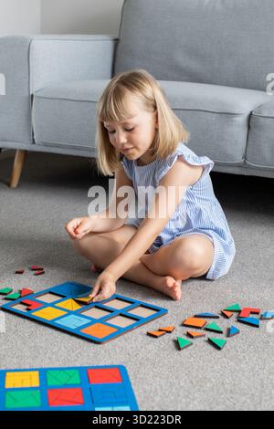 Une fille mignonne joue un jeu en bois logique sur le sol dans la chambre. Jouet éducatif. Banque D'Images