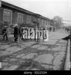URSS, RSS d'Ukraine, 1977. Sloviansk, oblast de Donetsk. Une grande brigade de travailleuses de l'usine d'armature et d'isolation (AIZ) participe à un « Subbotnik communiste » (une journée de travail volontaire non rémunéré). Les femmes, en manteaux et foulards, sont engagées dans un travail manuel lourd, nettoyant une cour d'usine très boueuse avec des balais et des pelles. En arrière-plan sont des ateliers d'usine et des piles de palettes en bois. Cette photo d'archive montre la réalité du travail collectif et de 'blagoustroystvo' (embellissement) à l'époque soviétique Banque D'Images