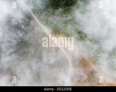 Vue par drone d'une route de montagne sinueuse coupant à travers la brume Banque D'Images