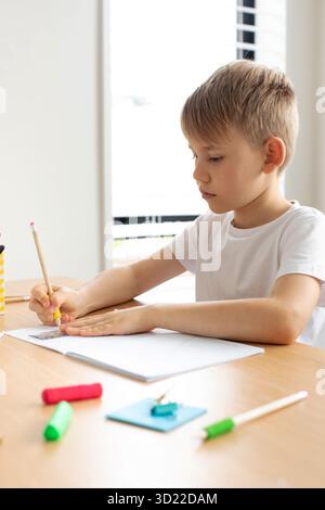 Un joli garçon fait un dessin avec une règle et un crayon. Leçons à la maison. Géométrie et dessin. Banque D'Images