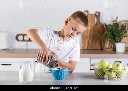 Le garçon verse les flocons de chocolat en conserve dans l'assiette.Petit déjeuner enfant. Banque D'Images
