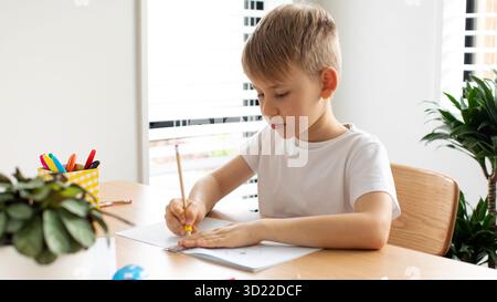 Un joli garçon fait un dessin avec une règle et un crayon. Leçons à la maison. Géométrie et dessin. Banque D'Images