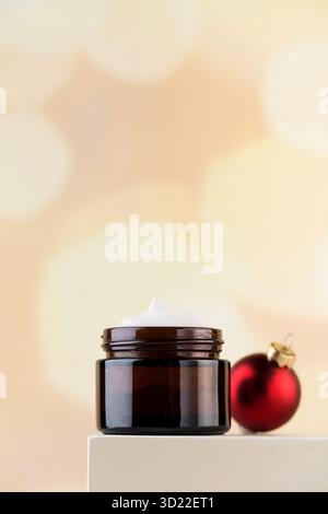 Crème nourrissante pour le visage sur un piédestal avec une boule de Noël. Le concept de cosmétiques pour les soins de la peau en hiver. Banque D'Images
