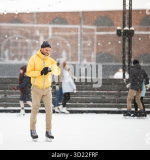 Joyeux homme d'âge moyen vérifiant la montre intelligente sur la patinoire, à l'extérieur dans la journée d'hiver enneigée Banque D'Images