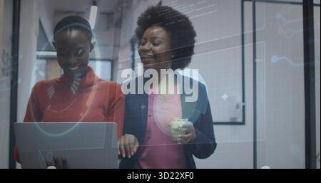 Deux femmes portant un pull et un blazer examinant le code dans le bureau avec ordinateur portable, tasse à café et hologramme Banque D'Images