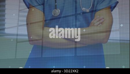 Médecin masculin debout croisant les bras dans le couloir portant des gommages, stéthoscope avec interface numérique Banque D'Images