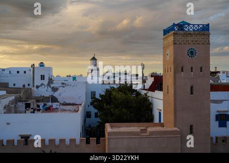 Coucher de soleil sur un paysage urbain historique avec des bâtiments blancs et une tour beige proéminente. Essaouira, Maroc Banque D'Images