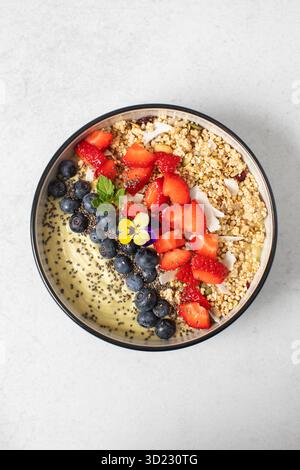 Bol à smoothie vert avec avocat, granola et baies. Végétarien, petit déjeuner sain. Banque D'Images
