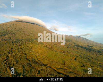 Flanc de montagne vert luxuriant avec des nuages roulant sur le sommet sous un ciel bleu. Lombok, Senaru, Indonésie Banque D'Images