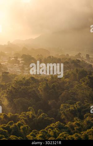 Forêt verdoyante et lever de soleil doré brumeux sur un village de montagne lointain. Lombok, Sembalun, Indonésie Banque D'Images