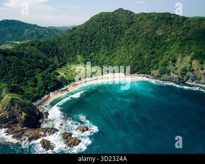 Vue aérienne d'une plage isolée entourée de collines verdoyantes et d'eaux turquoises. Pantai Telawas Beach, Mekar Sari, Praya Barat, Central Lombok Regency, West Nusa Tenggara, Indonésie Banque D'Images
