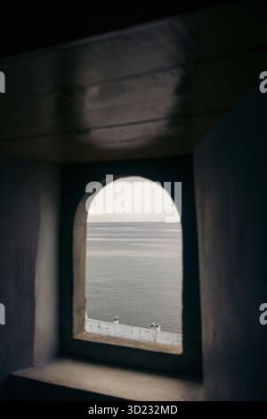 Vue sur la mer calme à travers une fenêtre voûtée, encadrée par des murs sombres dans un cadre serein. Ambon, Maluku, Indonésie Banque D'Images