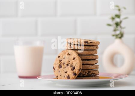 Les biscuits sont étalés sur une assiette, un verre de lait frais. Biscuits faits maison avec pépites de chocolat. Banque D'Images