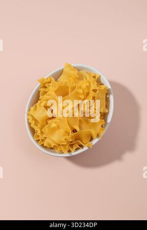 Vue de dessus des pâtes mafaldine dans un bol sur fond rose Banque D'Images