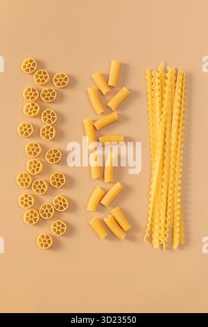 Assortiment de variétés de pâtes non cuites disposées en rangées sur un fond beige, présentant différentes formes Banque D'Images
