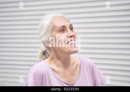 Femme caucasienne âgée souriant joyeusement dans le haut à pois rose clair contre Banque D'Images