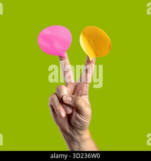 La main d'un homme caucasien fait un signe en V, tenant deux notes blanches et vides à bulles de discours (rose et jaune), isolées sur un fond vert vif. Banque D'Images