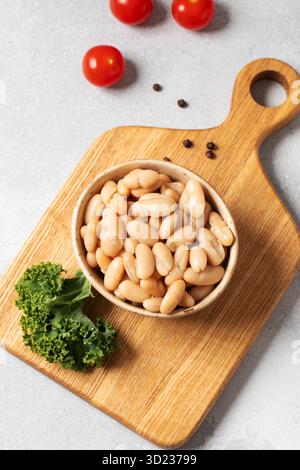 Haricots blancs en conserve dans un bol sur planche de bois pour la nourriture végétarienne riche en protéines végétales. Concept végétarien et de nourriture saine. Banque D'Images
