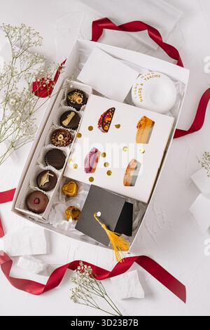 Un coffret cadeau magnifiquement agencé est rempli d'un assortiment de desserts, y compris des chocolats et des pâtisseries, entouré d'éléments décoratifs et de côtes Banque D'Images