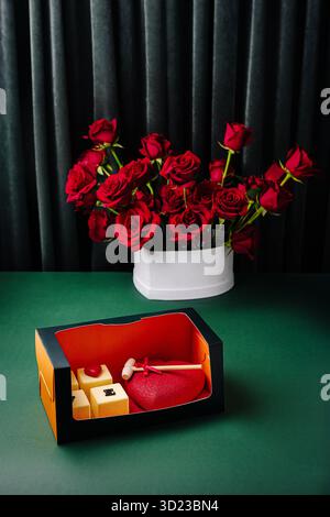 Coffret cadeau avec chocolats coeur et roses rouges sur une table verte Banque D'Images