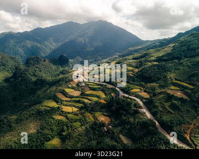 Vue aérienne de vallées verdoyantes avec des routes sinueuses et toile de fond de montagne sous un ciel nuageux. District de Nguyen BÏnh, Cao Bang, Vietnam Banque D'Images