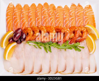 Un plateau de fruits de mer magnifiquement arrangé avec saumon finement coupé et filets de poisson blanc, accompagnés de crevettes grillées, oli Banque D'Images