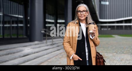 Femme caucasienne mature avec une tasse de café dans ses mains sur le fond du centre commercial Banque D'Images