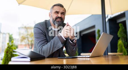 Portrait d'homme d'affaires sérieux avec ordinateur portable dans le café de la ville travaillant en ligne Banque D'Images
