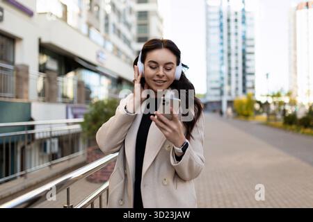 Une femme écoute de la musique dans la rue avec des écouteurs et regarde un téléphone portable Banque D'Images