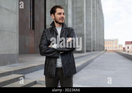Un jeune homme avec un sourire dans une paire croise ses bras sur sa poitrine à l'extérieur Banque D'Images