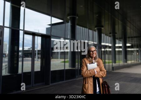 Femme d'affaires de cinquante ans avec une tablette dans les mains à l'entrée du centre d'affaires Banque D'Images