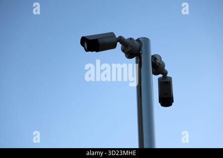 Deux caméras de sécurité sont montées sur un haut poteau blanc, faisant face à des directions différentes. L'image capture l'équipement de surveillance extérieur moderne contre un Banque D'Images