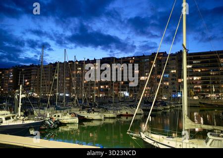 Bateaux amarrés à une marina avec les lumières de la ville se reflétant sur l'eau au crépuscule. Blankenberge, Flandre occidentale, Belgique Banque D'Images