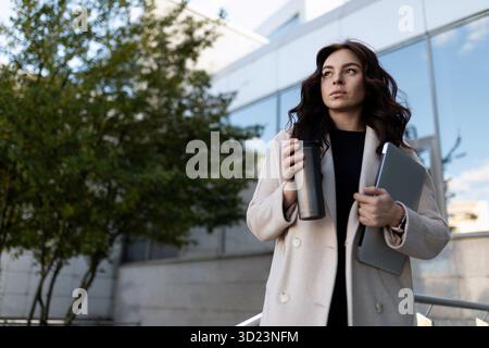 Femme d'affaires avec un ordinateur portable et un verre de café sur le fond du centre d'affaires, concept de croissance de carrière Banque D'Images